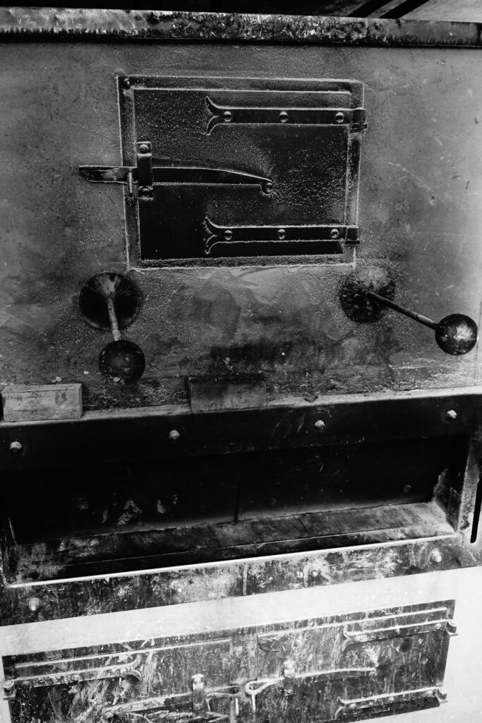Das Herzstück der Bäckerei: Detailaufnahme der massiven, gusseisernen Front eines historischen Backofens mit alten Hebeln und Scharnieren im Backhaus der Vielfalt.
