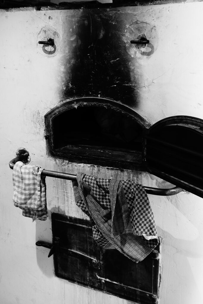 Authentische Backkultur: Die geöffnete Klappe eines traditionellen Holzbackofens mit Rußspuren und einem aufgehängten karierten Tuch im Backhaus der Vielfalt.