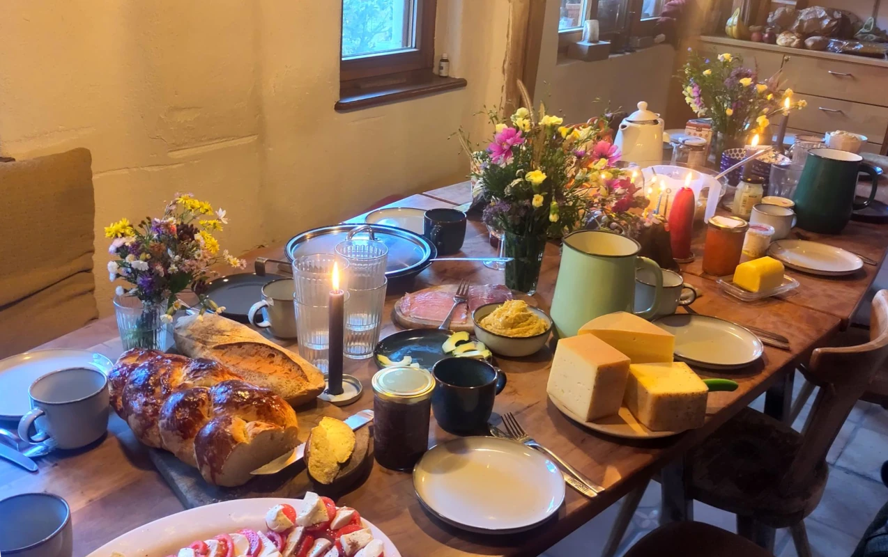 Vom Acker auf den Teller: Ein reich gedeckter Frühstückstisch mit hofeigenem Käse, frischem Brot und Wiesenblumen zeigt den Genuss und die Gemeinschaft im Luzernenhof.