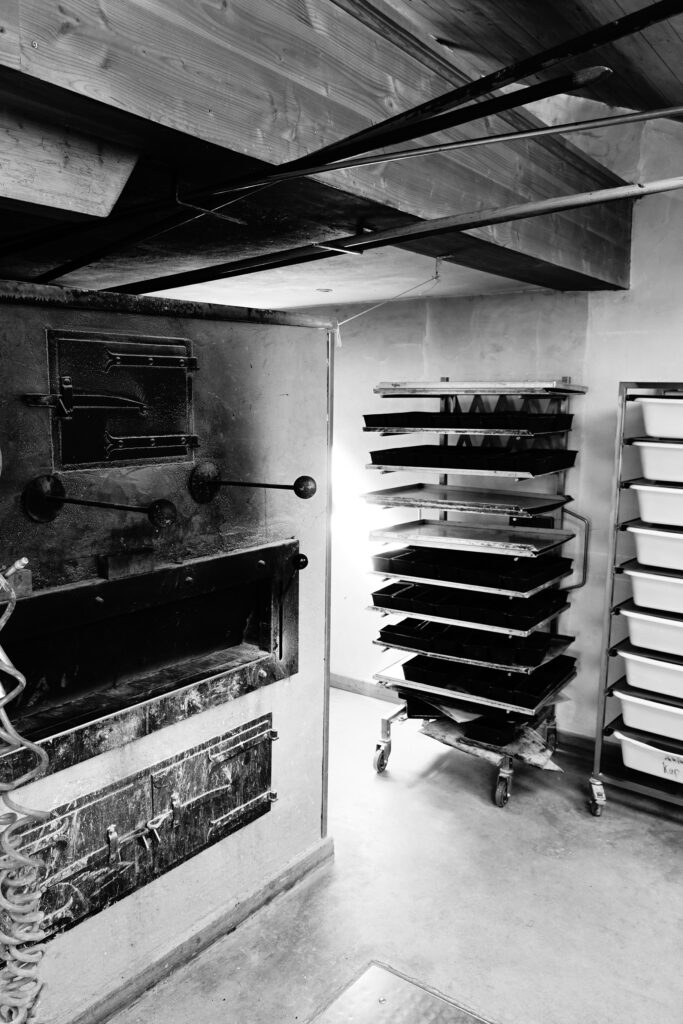 Traditionelles Handwerk im Backhaus der Vielfalt: Ein großer, uriger Backofen steht neben einem Stikkenwagen mit Blechen und Wannen in der gemütlichen Backstube.