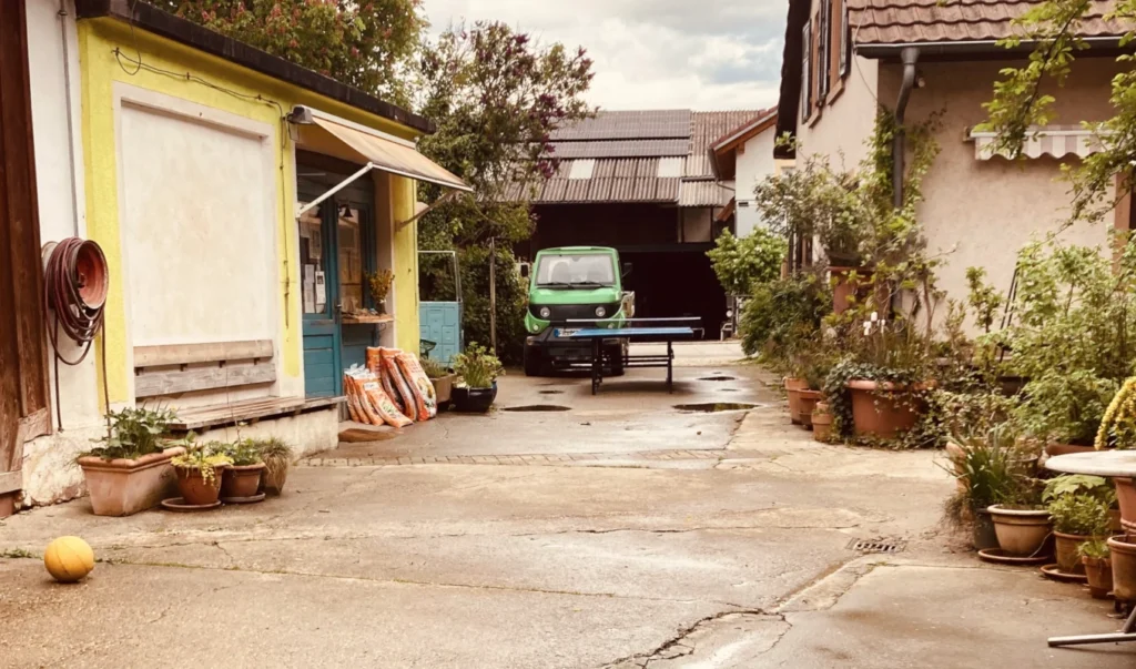 Einblick in den Hofalltag: Der gemütliche Innenhof der Solawi Luzernenhof mit Hofladen, Wirtschaftsgebäuden und einem grünen Lieferfahrzeug.