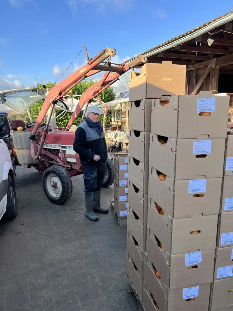 Kooperation in der Landwirtschaft: Ankunft der griechischen Orangenkisten auf einem lokalen Hof – ein Landwirt nimmt die Lieferung neben seinem roten Traktor entgegen.