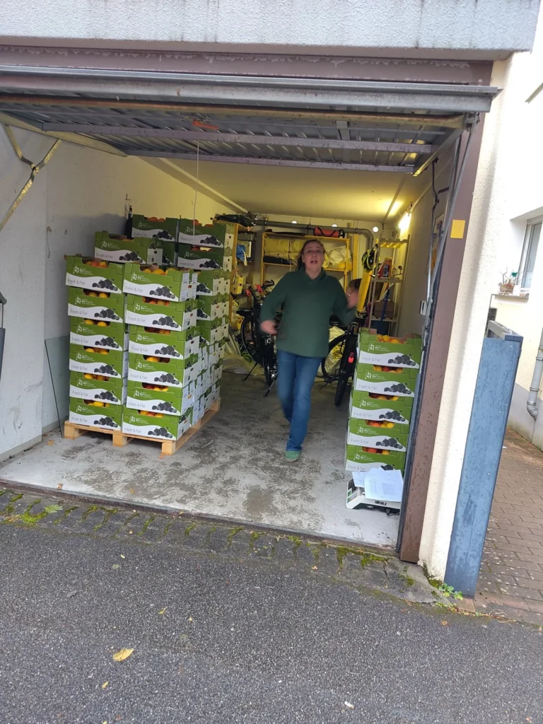 Die Community in Aktion: Ein privater Verteilpunkt in einer Garage in Deutschland, vollgestapelt mit grünen Teikei-Kisten, bereit zur Abholung durch die Mitglieder.