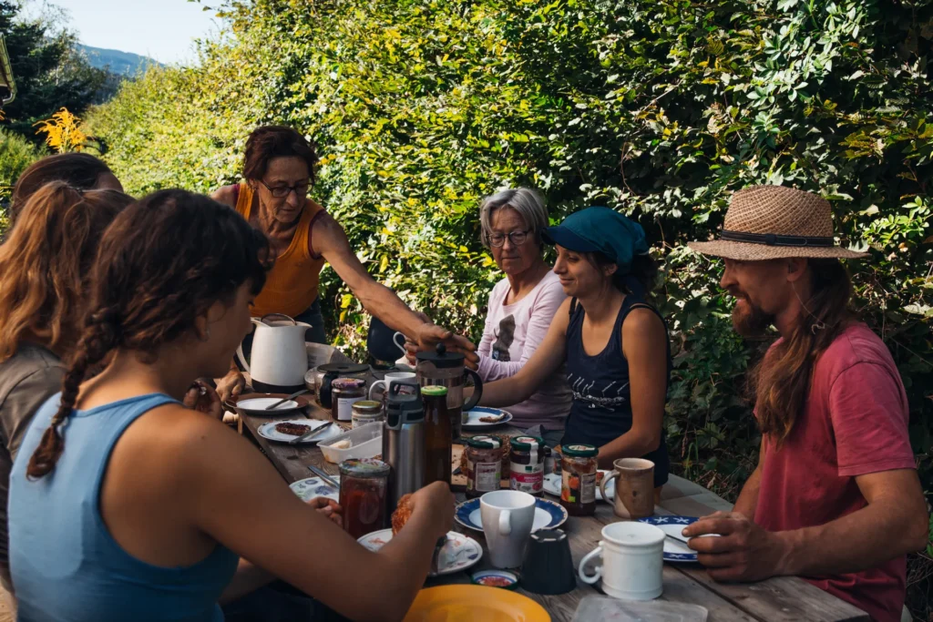 Gemeinsames Mittagessen im Grünen: Das Team des Lebensgarten Dreisamtal sitzt gemütlich an einem Holztisch zur Pause zusammen – gelebte Gemeinschaft in der Landwirtschaft.