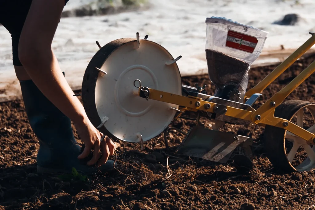 Präzisionsarbeit im Gemüsebau: Nahaufnahme einer mechanischen Sämaschine, die Saatgut exakt in den vorbereiteten Boden des Lebensgarten Dreisamtal einbringt.