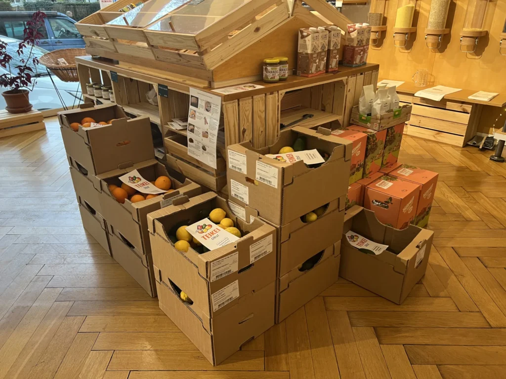 Teikei Abholstation: Ein gemütlicher Verteilpunkt in einem Laden mit gestapelten Kisten voller frischer Bio-Orangen und Zitronen, bereit zur Abholung durch die Mitglieder.