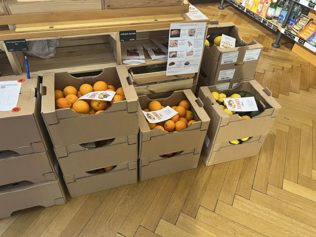 Transparenter Direkthandel zum Anfassen: Geöffnete Kisten mit Teikei-Orangen und Zitronen stehen in einem Abholpunkt (Depot) auf Holzkisten präsentiert.