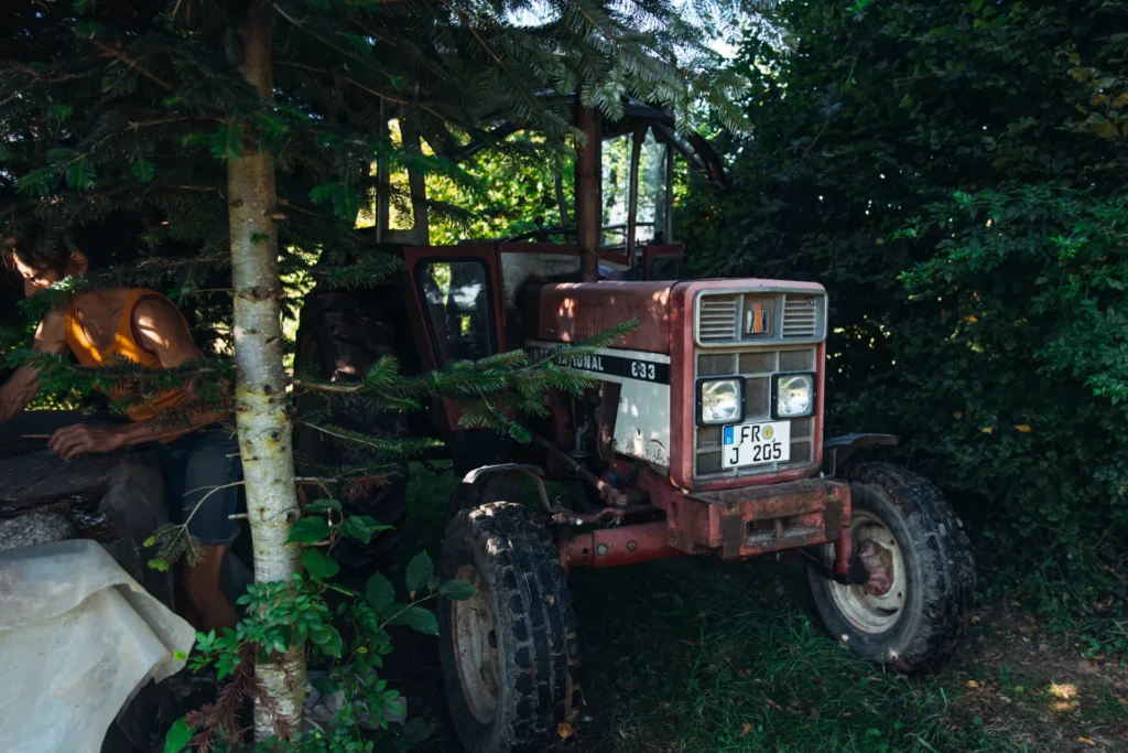 Traditionelle Landtechnik: Ein roter International Traktor steht im Halbschatten am Feldrand der Solawi Lebensgarten Dreisamtal bereit für den Einsatz.